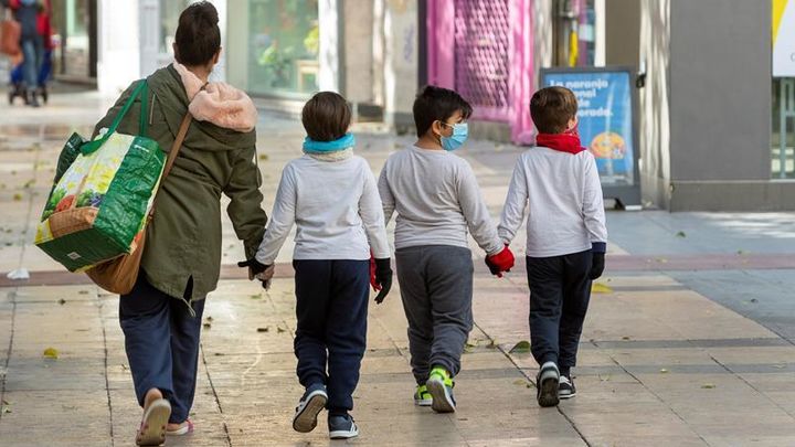 Tres niños caminan por la calle junto a una persona adulta / EFE
